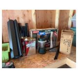 Camping treasures, including rollout camp table, Coleman gas stove, battery powered lantern, two cans of camping fuel, life preserver jacket, and hatchet