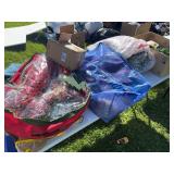 Bags and boxes of Christmas decor, including lighted garland, wreaths, tree holder
