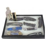 A Collection of Nine Folding Knives with a Vintage WIN Lighter and Antique Glass Bottle in a Display Case