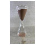 A clear glass hourglass with pink sand