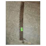 vintage two-man crosscut saw, or 'misery whip,' features a long, rusted steel blade and a single, detachable wooden handle