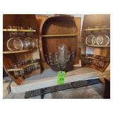 Mid-Century Karoff barrel wall cabinet features a folding design with brass accents and includes a collection of glassware. To be mounted on a wall