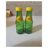 vintage green glass Squirt soda bottle salt and pepper shakers. They feature yellow plastic screw-on caps, replicating the iconic soda bottles from the 1950s or 1960s.